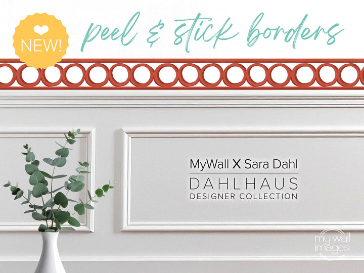 a white wall with a decorative border, a vase of greenery, and text that reads &quot;MyWall X Sara Dahl Dahlhaus Designer Collection&quot;.