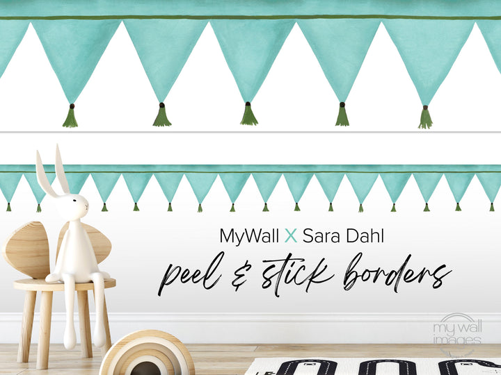a white rabbit sitting on a wooden chair, with a wall decorated with green triangular banners and tassels. The wall has a text overlay that reads &quot;MyWall x Sara Dahl Peel & Stick Borders&quot;.