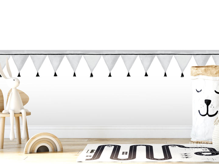 A white rabbit sits on a wooden chair in a room with a white wall, a black and white tasseled banner, a wooden floor, and a toy car.