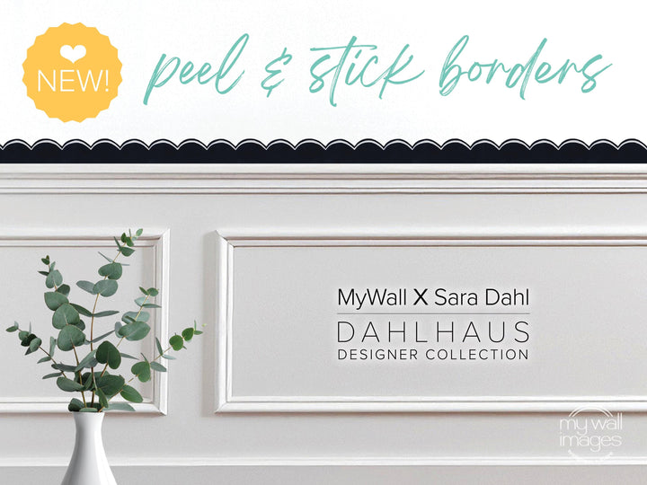 a white wall with a framed picture of a plant, and there is text that reads "MyWall x Sara Dahl Dahlhaus Designer Collection" and "NEW!" in the top left corner.