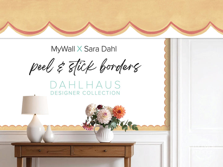 a wooden table with a vase of flowers, a lamp, and a window with a decorative border. The text overlay includes the names MyWall X Sara Dahl and the phrase &quot; Peel & Stick Bordered&quot; in a decorative font.