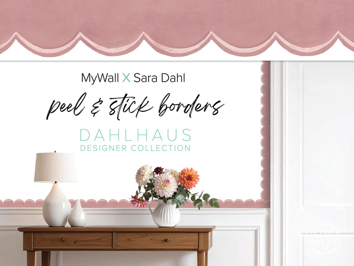 a wooden table with a vase of flowers, a lamp, and a pink decorative border on the wall behind it.