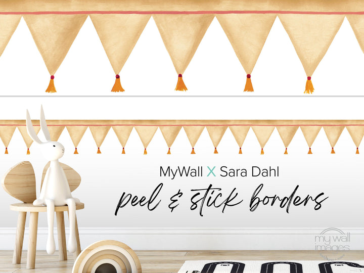 a white rabbit sitting on a wooden chair, with a wall decorated with orange and white tassels. The wall has a text overlay that reads &quot;MyWall x Sara Dahl Peel & Stick Borders&quot;.